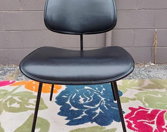 May include: A black chair featuring a curved, padded backrest and a matching contoured seat. The chair is supported by four thin, dark metal legs that angle outward, providing a stable base for the smooth, solid black upholstery on the seat.