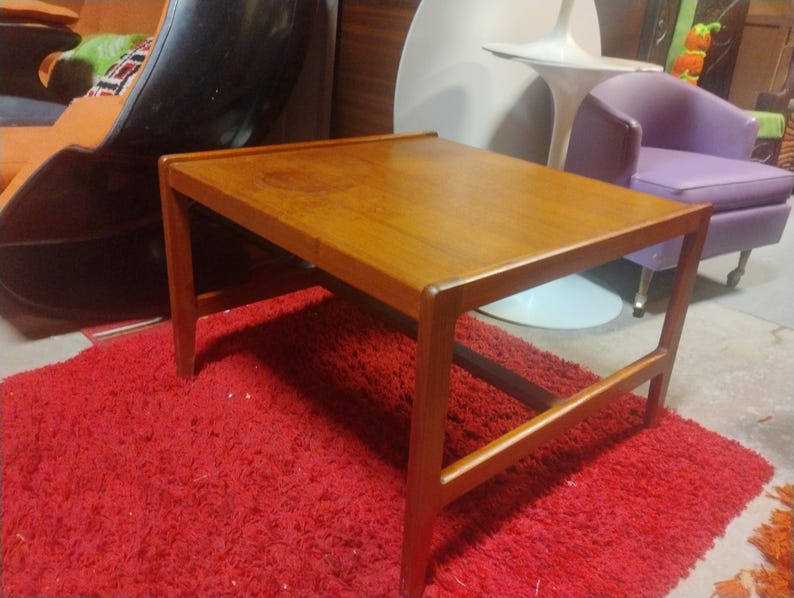 May include: A rectangular wooden coffee table with a light brown finish. The table has a simple design with a flat top and four legs. The table is sitting on a red shag rug.