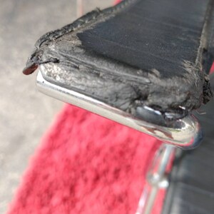 May include: Close-up of a black leather chair with a chrome frame. The leather is worn and shows signs of age. The chair is sitting on a red rug.