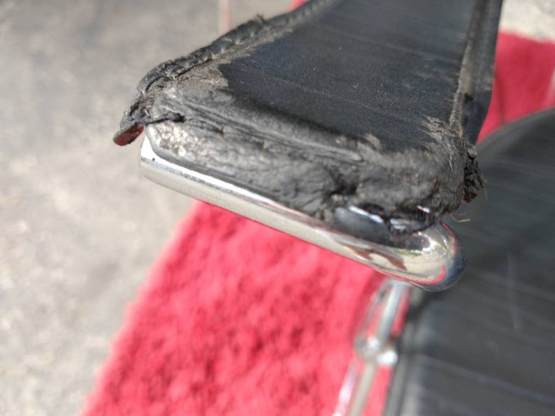 May include: Close-up of a black leather chair with a chrome frame. The leather is worn and shows signs of age. The chair is sitting on a red rug.