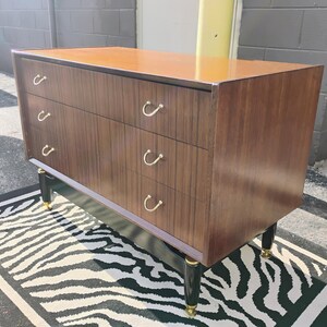 May include: A dark brown wooden dresser with four drawers and black legs. The drawers have gold metal handles. The dresser is sitting on a black and white zebra print rug.