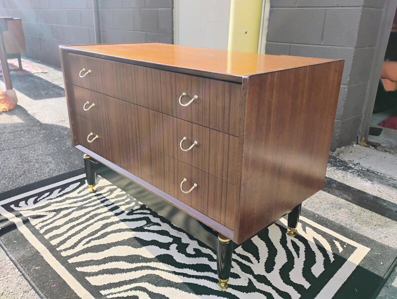 May include: A dark brown wooden dresser with four drawers and black legs. The drawers have gold metal handles. The dresser is sitting on a black and white zebra print rug.