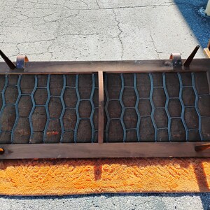 May include: A rectangular, mid-century modern speaker cover with a dark wood frame. The speaker cover has a brown mesh interior with a blue-gray honeycomb pattern. The cover is resting on an orange rug.