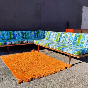 May include: Two-piece mid-century modern sofa with a geometric blue, green, and white patterned fabric. The sofa has a wooden frame and legs. An orange shag rug is in front of the sofa.