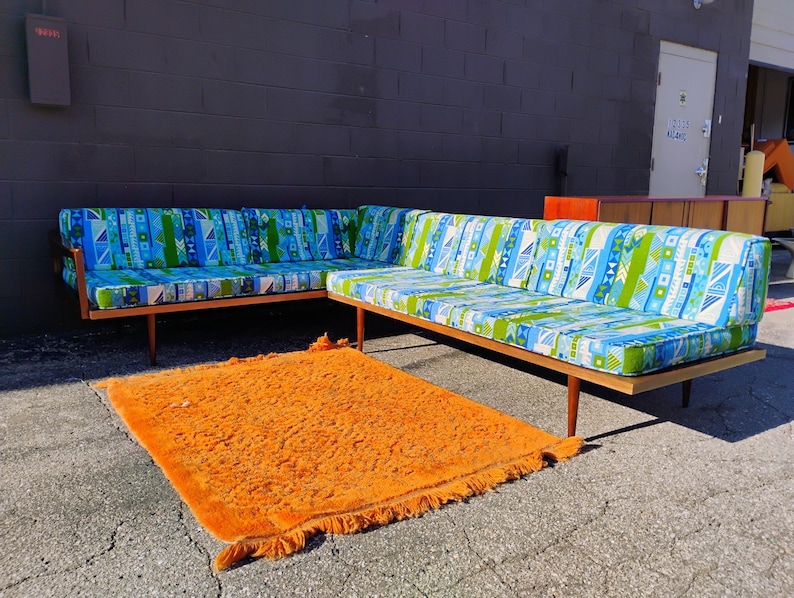 May include: Two-piece mid-century modern sofa with a geometric blue, green, and white patterned fabric. The sofa has a wooden frame and legs. An orange shag rug is in front of the sofa.