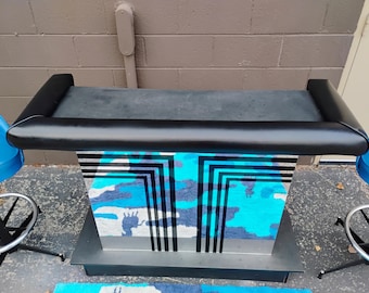 May include: A black bar with a padded top and a mirrored base with a geometric pattern in black and blue. The bar is sitting on a rug with a similar pattern.