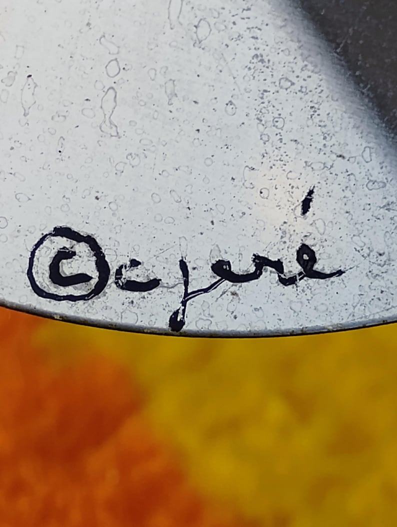 May include: A metallic surface featuring a black handwritten signature that reads C. Jere with a copyright symbol enclosed in a circle to the left. The surface has a slightly speckled texture and a reflective quality under the light.