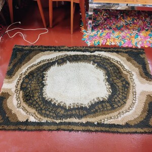 May include: A brown, beige and black shag rug with a large, white, circular design in the centre. The rug has a shaggy texture and a modern, abstract design.