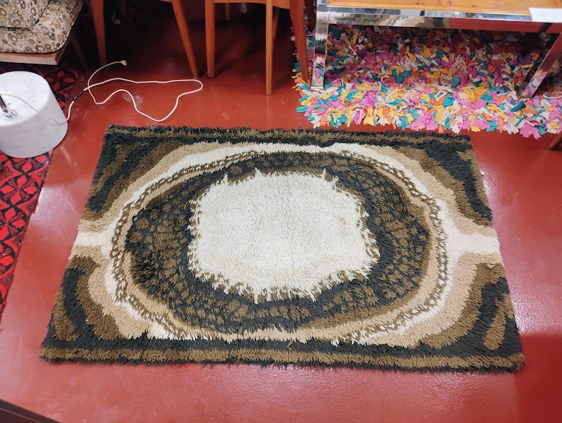 May include: A brown, beige and black shag rug with a large, white, circular design in the centre. The rug has a shaggy texture and a modern, abstract design.