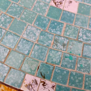 Op de afbeelding: Een close-up van een turquoise moza&iuml;ek tegel oppervlak met witte en lichtblauwe accenten. De tegels zijn in een verspringend patroon gerangschikt, waardoor een getextureerd en visueel aantrekkelijk oppervlak ontstaat.