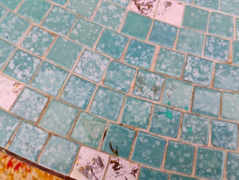 Op de afbeelding: Een close-up van een turquoise moza&iuml;ek tegel oppervlak met witte en lichtblauwe accenten. De tegels zijn in een verspringend patroon gerangschikt, waardoor een getextureerd en visueel aantrekkelijk oppervlak ontstaat.