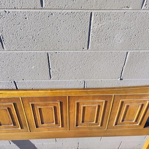 May include: A wooden headboard with a geometric design. The headboard is made of light brown wood and has a rectangular shape. The headboard is in good condition and has no visible damage.