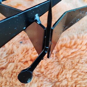 May include: Close-up of a black metal object with sharp, angular shapes. The object appears to be a decorative or functional piece, possibly a component of a larger structure. The metal has a glossy finish.