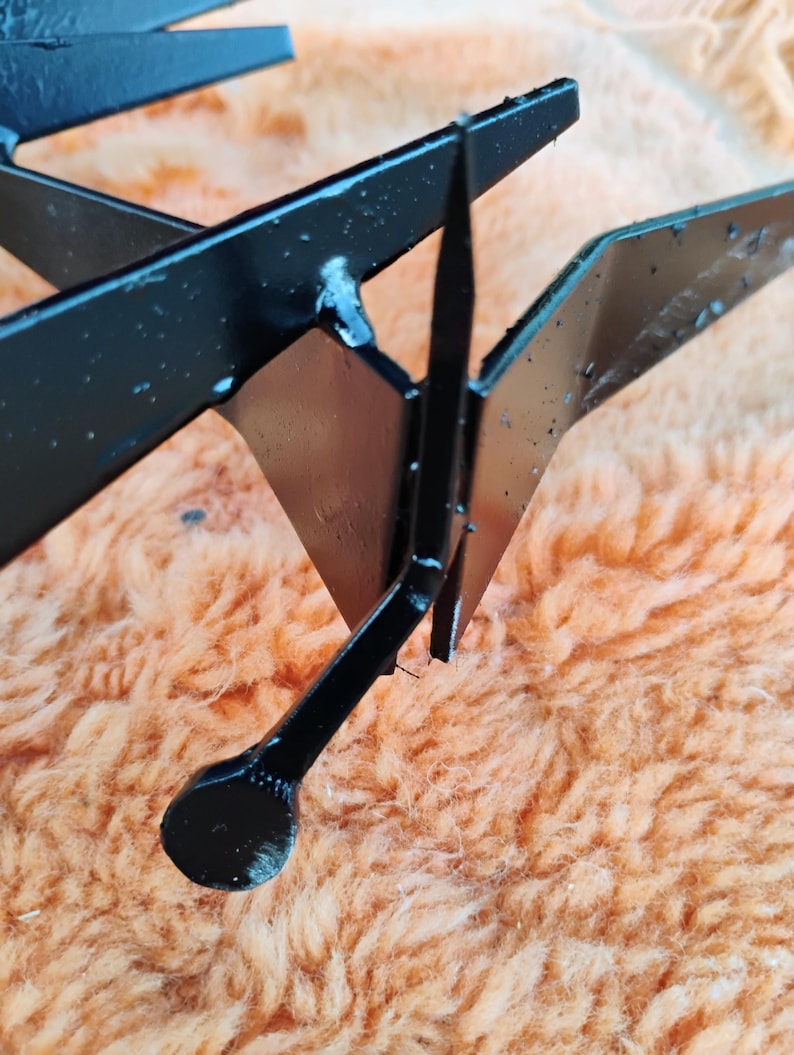 May include: Close-up of a black metal object with sharp, angular shapes. The object appears to be a decorative or functional piece, possibly a component of a larger structure. The metal has a glossy finish.
