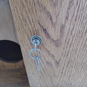 May include: Close-up of a wooden cabinet door with a key in the lock. The door has a natural wood grain pattern. The key is silver and attached to a small key ring.