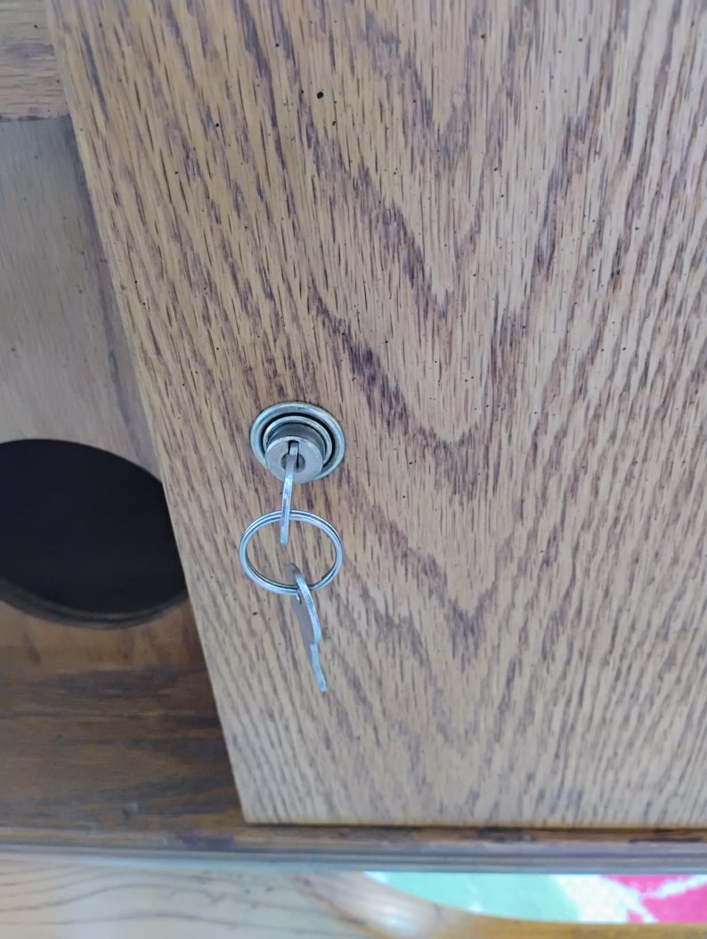 May include: Close-up of a wooden cabinet door with a key in the lock. The door has a natural wood grain pattern. The key is silver and attached to a small key ring.