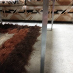 May include: A brown and white patterned sofa with a shaggy brown and white rug. The sofa has a geometric design. The rug is on a concrete floor. The legs of the sofa are silver.