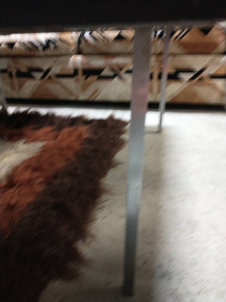 May include: A brown and white patterned sofa with a shaggy brown and white rug. The sofa has a geometric design. The rug is on a concrete floor. The legs of the sofa are silver.