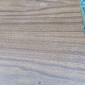 May include: A rectangular panel with a brown wood grain finish featuring two small, circular pre-drilled holes positioned vertically along the surface. The material displays a consistent dark brown pattern with lighter brown wood grain lines.