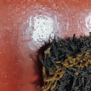 May include: Close-up of a red surface with white paint splatters. A black and brown fuzzy object is in the bottom right corner of the image.