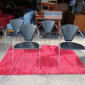May include: Four black leather chairs with chrome frames and curved arms. The chairs are arranged in a row on a red shag rug.