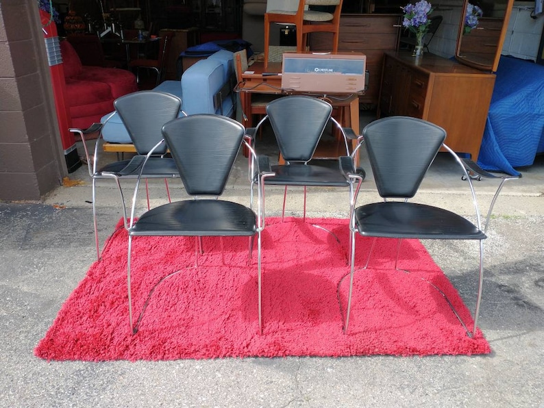 May include: Four black leather chairs with chrome frames and curved arms. The chairs are arranged in a row on a red shag rug.
