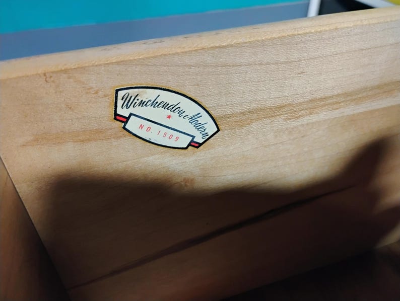 May include: Close-up of a light-colored wooden drawer with a label. The label reads "Winchendon Modern" in black script, with a red and white border, and the number "NO. 1509".