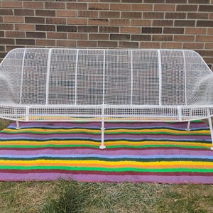 May include: A white metal sofa featuring a grid-patterned wire mesh construction. The sofa has a curved backrest, integrated armrests, and is supported by six thin, angled metal legs. The frame is finished in a smooth, solid white coating.