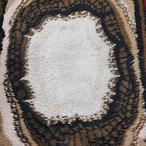 May include: A round, fluffy rug with a white centre and concentric rings of brown, beige, and black. The rug has a shaggy texture.