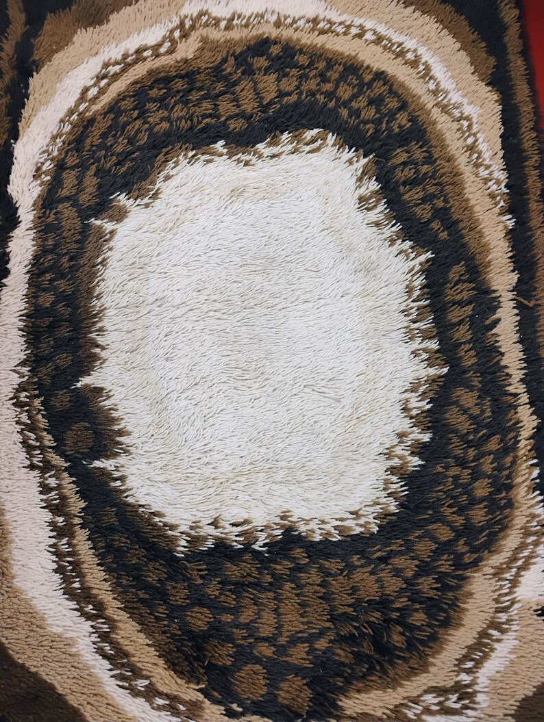 May include: A round, fluffy rug with a white centre and concentric rings of brown, beige, and black. The rug has a shaggy texture.