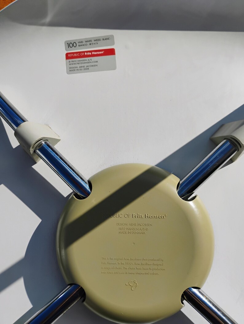 K&ouml;nnte beinhalten: Unterseite eines hellgr&uuml;nen Stuhlsitzes mit Chrombeinen. Der Stuhl ist mit "REPUBLIC OF Fritz Hansen" und "DESIGN ARNE JACOBSEN" gekennzeichnet. Der Stuhl wird in D&auml;nemark hergestellt.