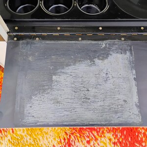 May include: A black metal bar cart with a black top and a silver metal frame. The top has a removable tray that is covered in a black material. The tray has a white, faded, and worn surface.