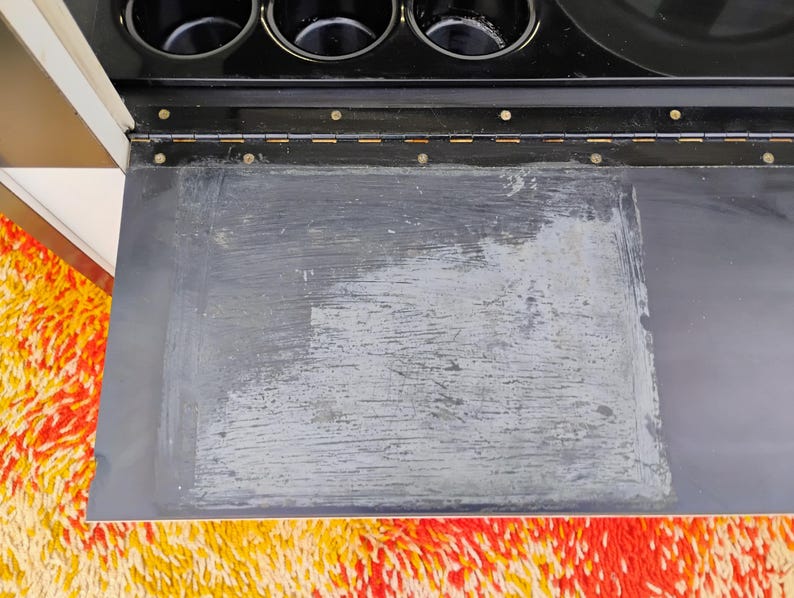 May include: A black metal bar cart with a black top and a silver metal frame. The top has a removable tray that is covered in a black material. The tray has a white, faded, and worn surface.
