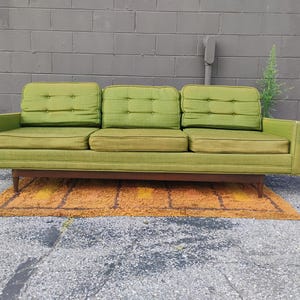 May include: A three-seat sofa upholstered in lime green fabric featuring three tufted back cushions and three matching seat cushions. The sofa is supported by a dark brown wooden frame with tapered legs, showcasing a linear and structured design.