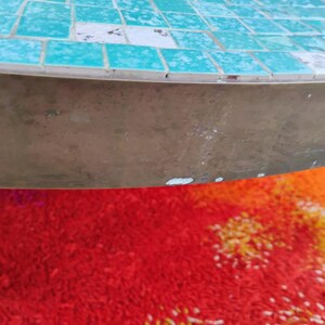 Op de afbeelding: Een ronde, turquoise moza&iuml;ek tafelblad met een messing onderstel. Het tafelblad is gemaakt van kleine, vierkante tegels. Het onderstel is een massief, glad messing stuk.