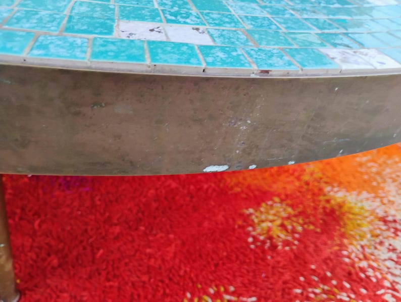 Op de afbeelding: Een ronde, turquoise moza&iuml;ek tafelblad met een messing onderstel. Het tafelblad is gemaakt van kleine, vierkante tegels. Het onderstel is een massief, glad messing stuk.