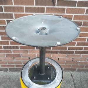 May include: A metal ashtray with a yellow base and a silver top. The top is round and has a funnel shape in the center. The base is a cylinder with a raised ring around the top.