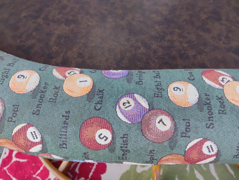 May include: Close-up of a section of a pool table. The fabric is green with images of billiard balls and words like "Pool", "Snooker", and "Billiards". The balls are numbered and colored.