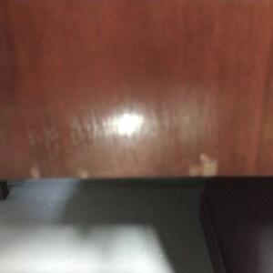 Pu&ograve; includere: Primo piano di una superficie in legno marrone scuro con alcuni segni chiari. La superficie sembra essere parte di un mobile.