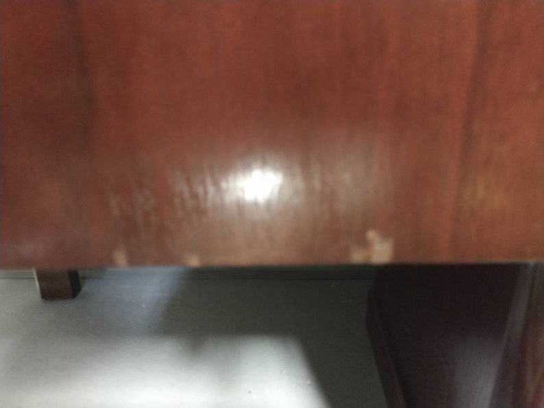 Pu&ograve; includere: Primo piano di una superficie in legno marrone scuro con alcuni segni chiari. La superficie sembra essere parte di un mobile.
