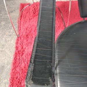 May include: Close-up of a black leather chair armrest with stitching detail. The armrest is made of a thick, durable material and has a slightly worn appearance.