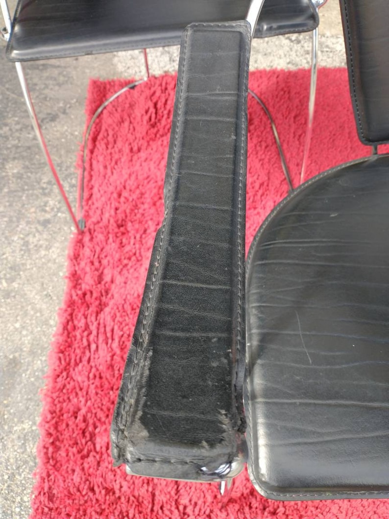 May include: Close-up of a black leather chair armrest with stitching detail. The armrest is made of a thick, durable material and has a slightly worn appearance.