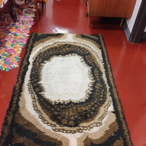 May include: A brown, beige and white shag rug with a large oval in the centre. The rug has a modern, abstract design.