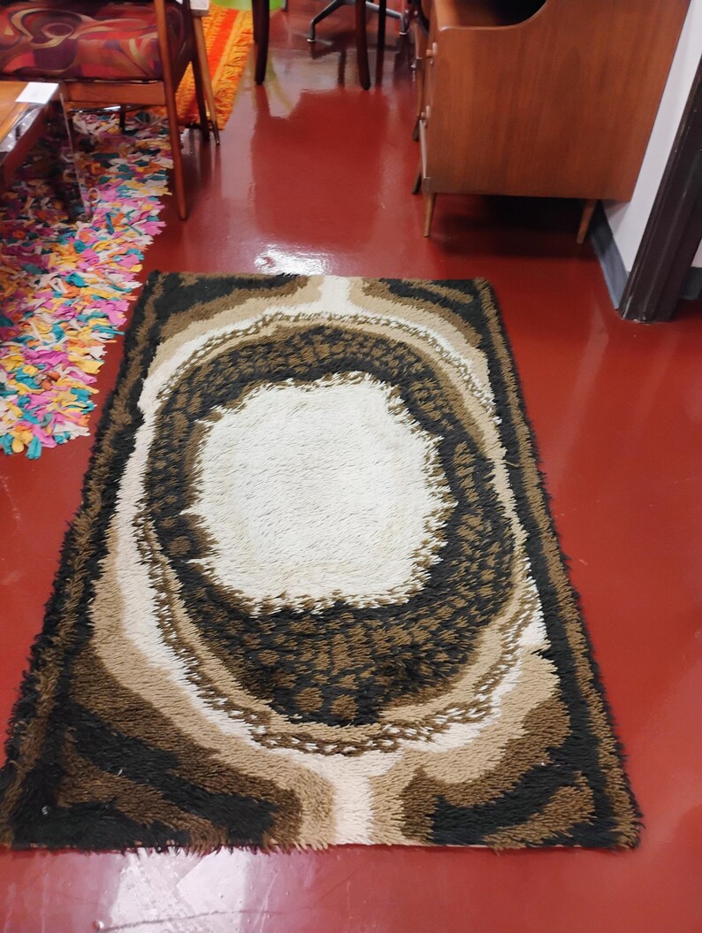 May include: A brown, beige and white shag rug with a large oval in the centre. The rug has a modern, abstract design.