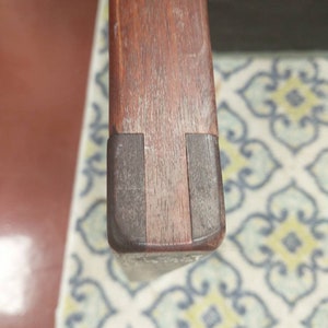 K&ouml;nnte beinhalten: Nahaufnahme der Oberseite einer Holzstuhlarmlehne. Die Armlehne ist aus dunklem Holz mit einer hellbraunen Beize. Die Armlehne ist leicht abgenutzt und hat ein paar Kratzer.