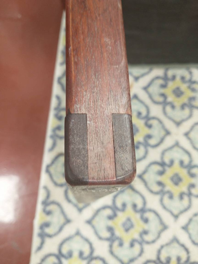 K&ouml;nnte beinhalten: Nahaufnahme der Oberseite einer Holzstuhlarmlehne. Die Armlehne ist aus dunklem Holz mit einer hellbraunen Beize. Die Armlehne ist leicht abgenutzt und hat ein paar Kratzer.