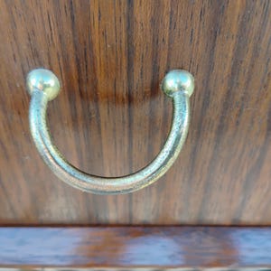May include: A close-up of a wooden cabinet door with a metal handle. The handle is a simple, rounded U-shape with a smooth, polished finish.