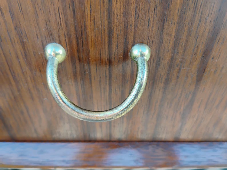 May include: A close-up of a wooden cabinet door with a metal handle. The handle is a simple, rounded U-shape with a smooth, polished finish.