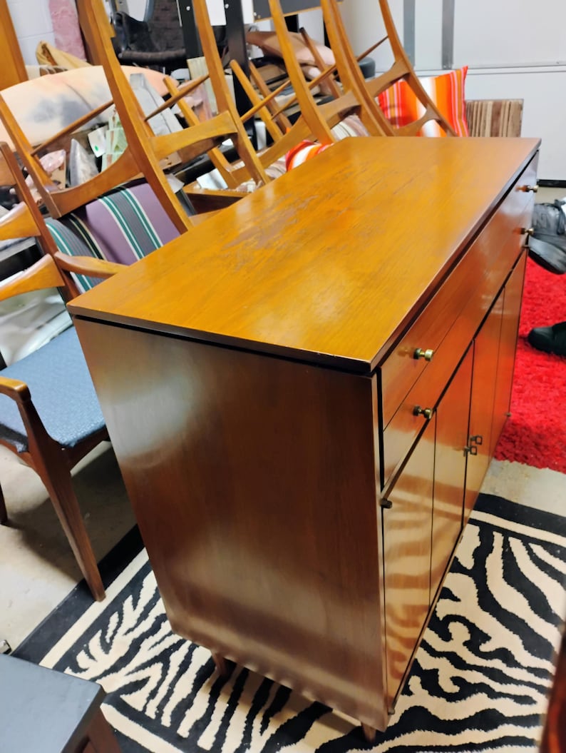 Puede incluir: Un armario de madera vintage con dos puertas y dos cajones. El armario tiene un acabado en madera clara y herrajes de lat&oacute;n. El armario est&aacute; sobre una alfombra de cebra de rayas blancas y negras.