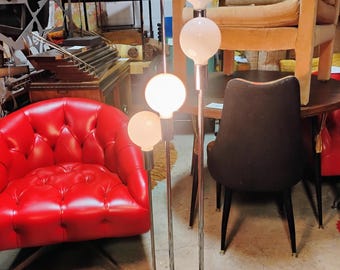Könnte beinhalten: Vintage Stehlampe mit vier weißen Kugelleuchten an Chromstielen. Die Lampe hat einen schwarzen kreisförmigen Sockel. Der Raum enthält einen roten Ledersessel und einen schwarz-weißen Zebra-Teppich, typisch für das Design der Jahrhundertmitte.